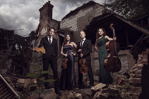 The quartet members, in evening dress, posed holding their instruments, whilst standing on the rubble of a ruined building