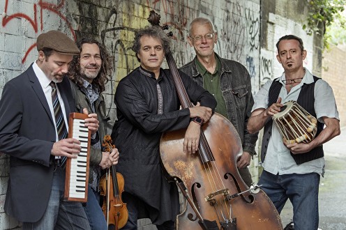 Moishe's Bagel standing with their instruments against a graffiti-covered wall