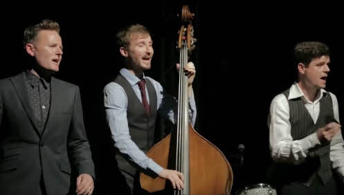 Joe Stilgoe standing left and singing, a bass player centre and percussionist to the right
