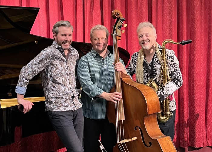 Four musicians from the Acoustic Triangle group standing by the piano and holding instruments