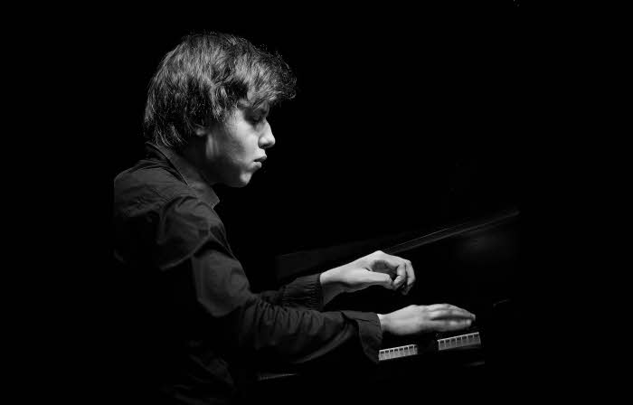 A close-up of Nikita at the keyboard, his right hand plays whilst his left hand is suspended over the keys.