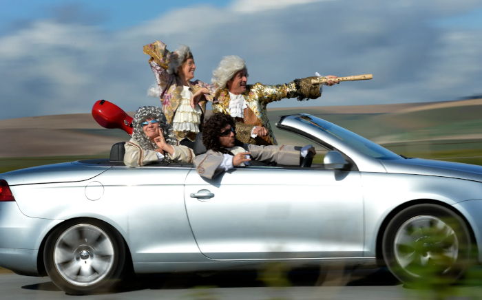The four members of Red priest, dressed in Baroque costume pose in a sleek, silver open-topped sports car